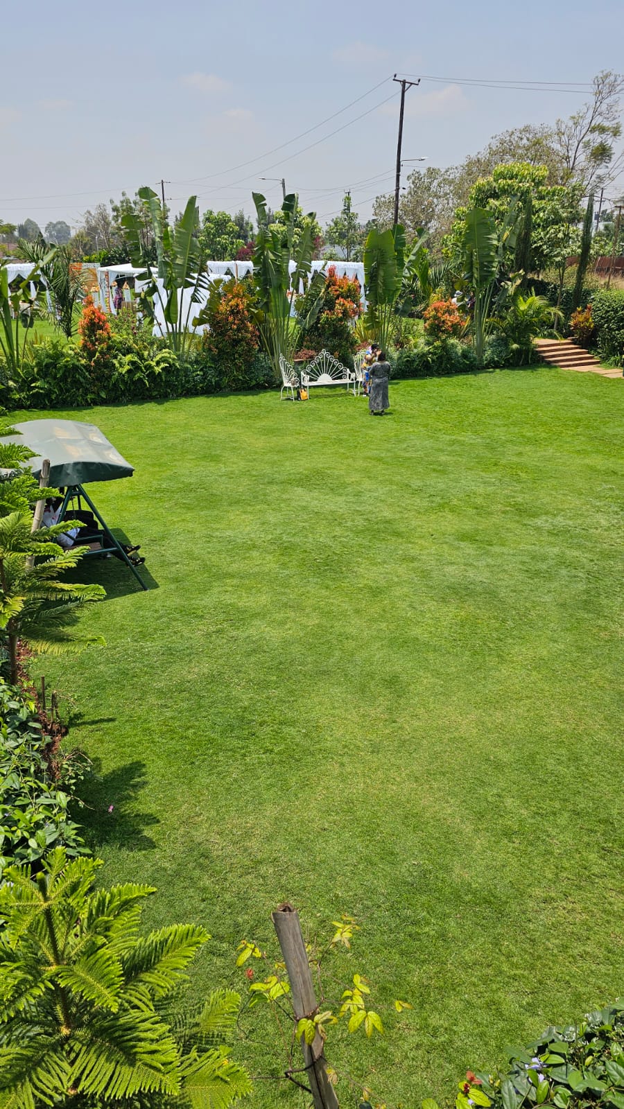 Elevated view across the garden lawn with a swing seat, garden bench and event canopies beyond