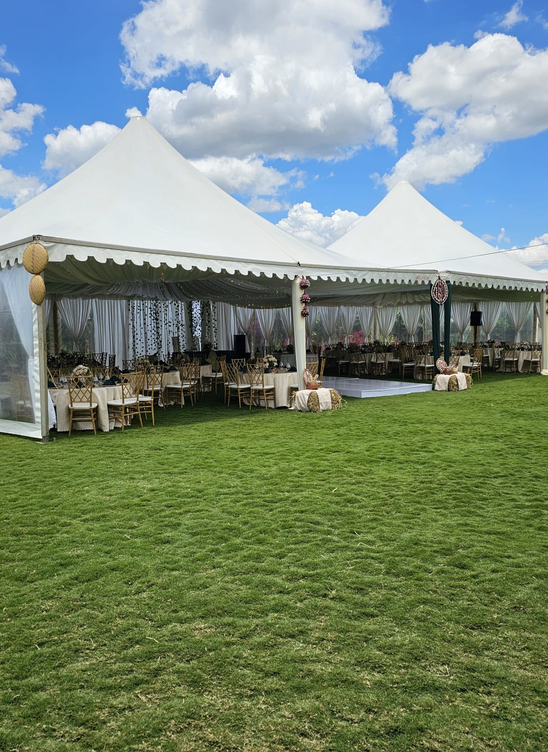 White peaked marquee with gold chiavari chairs and a dance floor open onto the green lawn